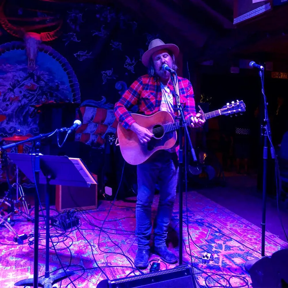 Brad Byrd singing with an acoustic guitar on the rug-covered stage at Pappy and Harriet's in Pioneertown