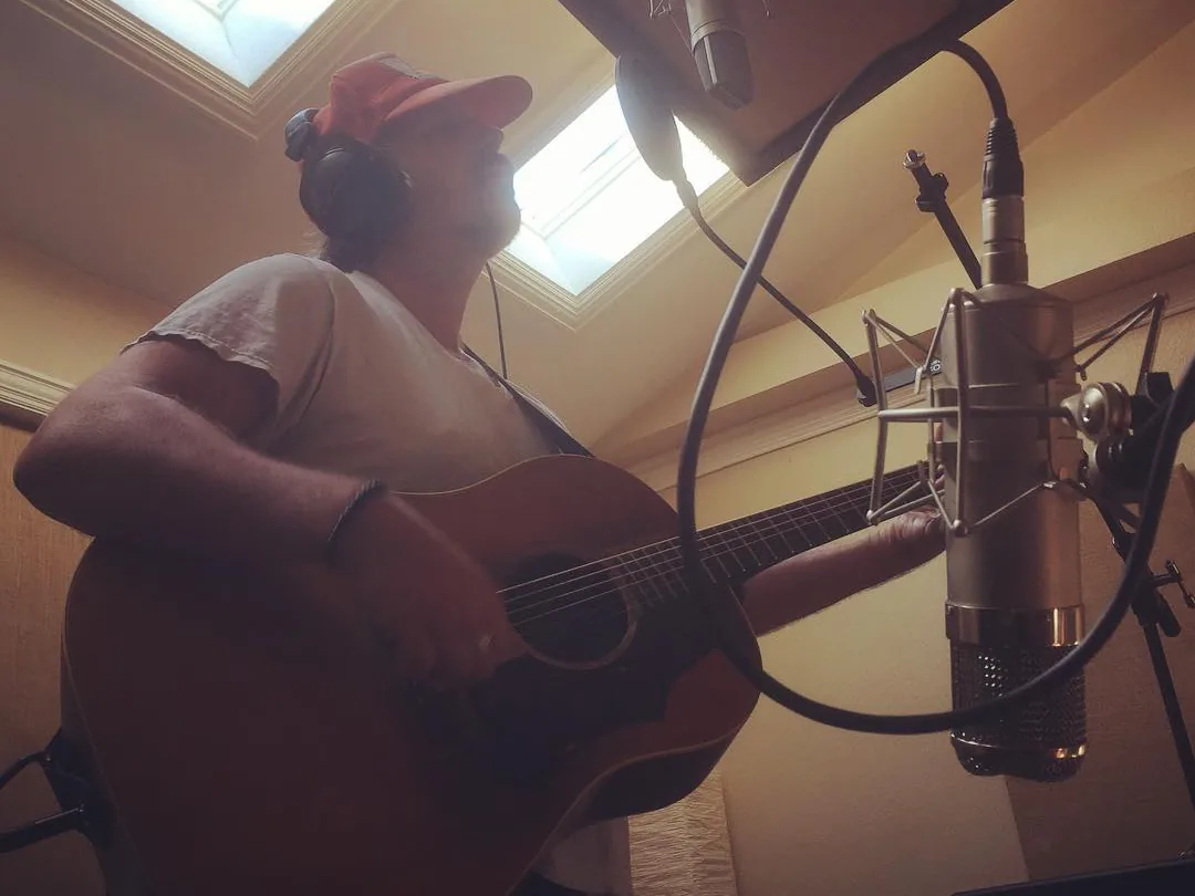 Brad Byrd in headphones recording acoustic guitar and vocals at a studio microphone